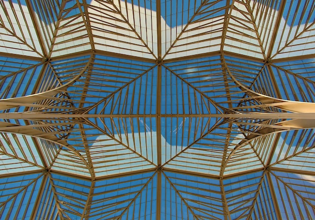 Lots of gold-colored beams in the ceiling of a building in Lisbon, Porgugal with a blue sky behind them
