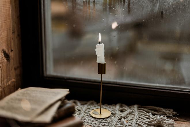 A small lit candle in a candle holder in front of a frosted window