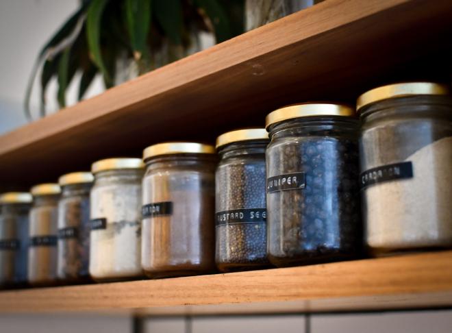 Glass jars of herbs on a shelf with labels of their contents